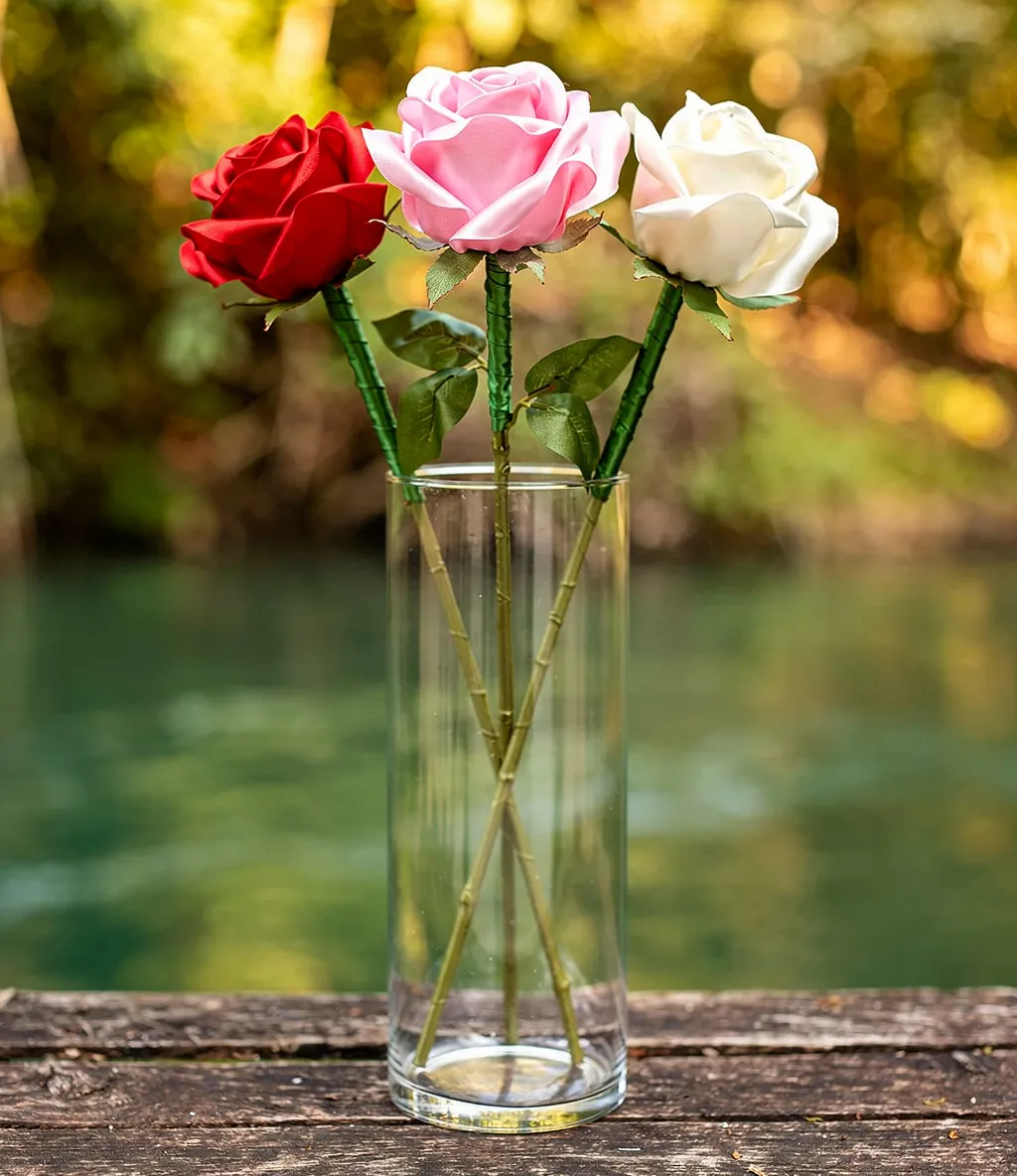 Three satin ribbon roses in red, pink, and white displayed in a clear glass vase.
