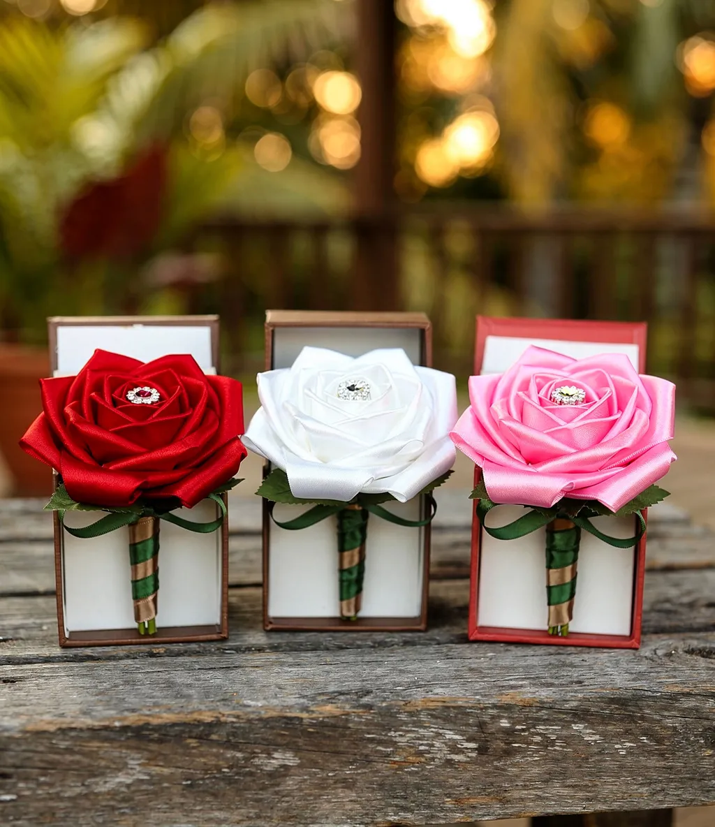 Three satin ribbon roses in red, white, and pink presented individually in small wooden boxes.